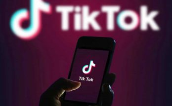 Mano che tiene telefono con aperto TikTok e sullo sfondo logo di TikTok