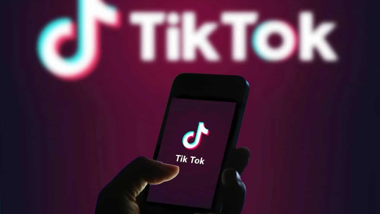 Mano che tiene telefono con aperto TikTok e sullo sfondo logo di TikTok