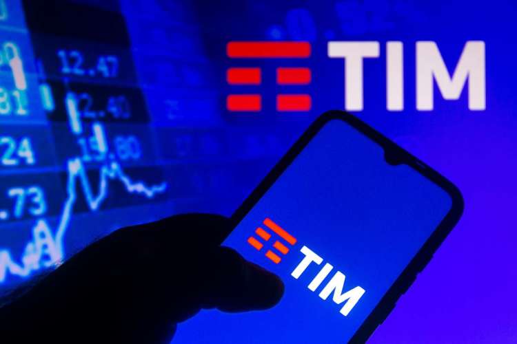 telefono in mano con logo Tim sullo schermo e sullo sfondo immagine