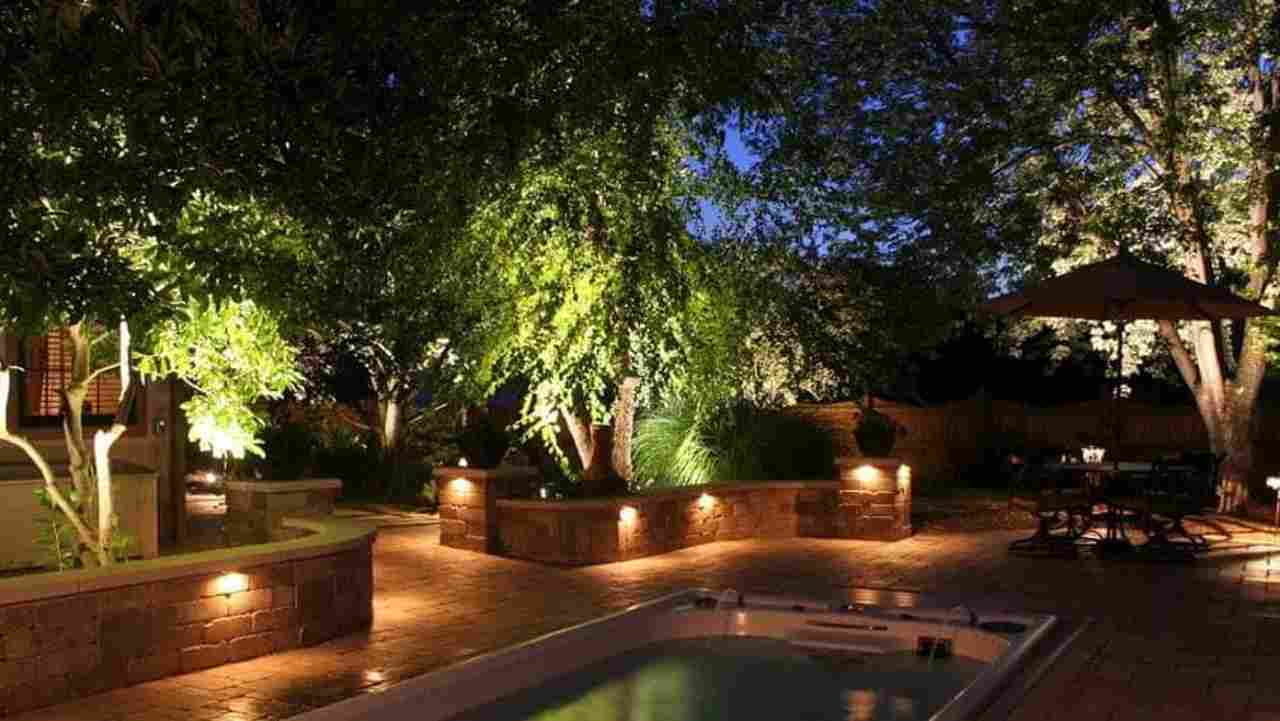 giardino con piante e piscina illuminato da luci per esterni la sera