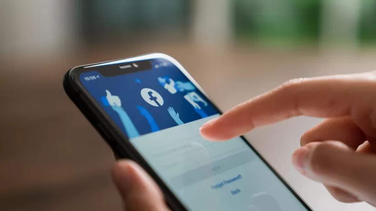 uomo tiene in mano il telefono mentre accede a Facebook