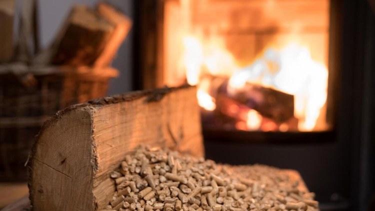 tronco di legno con affianco mucchietto di pellet con in sfondo stufa a pellet accesa