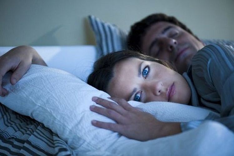 Woman in bed can't sleep while the man behind her does