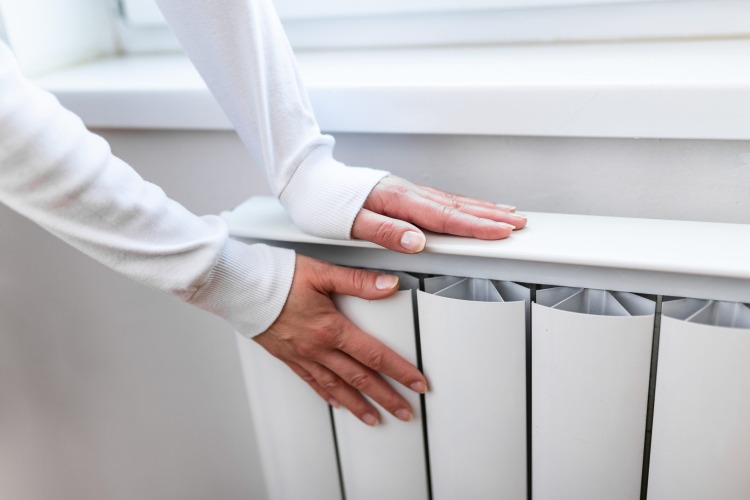 Donna si scalda le mani sul termosifone caldo